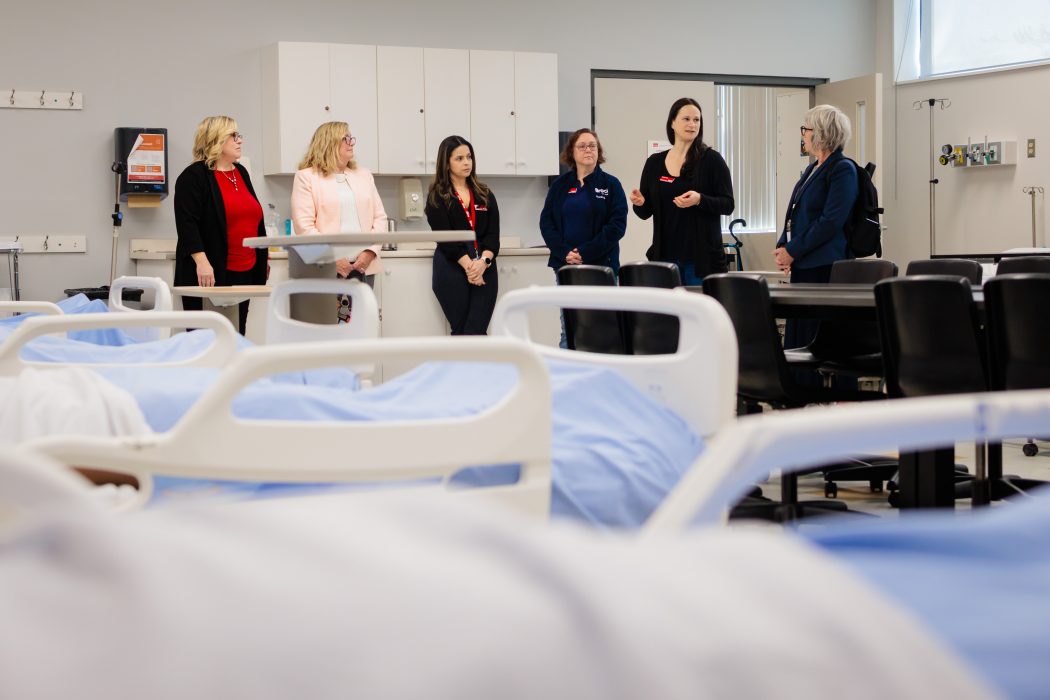 Six people stand in a row in nursing lab at a university.