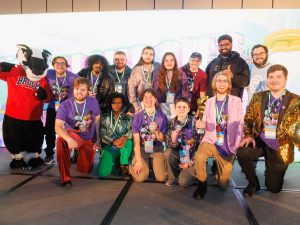 A group of students in matching theme outfits stand on a stage holding an award.