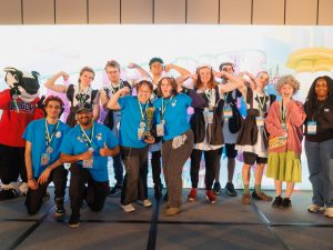 A group of students in matching theme outfits stand on a stage holding an award.