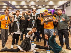 A group of students wearing various costumes, some dressed like maids, stand together in various poses smiling at the camera.