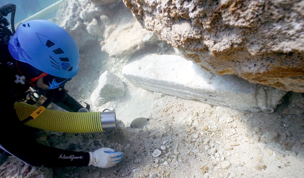 A person dives underwater excavating materials from the ocean floor.