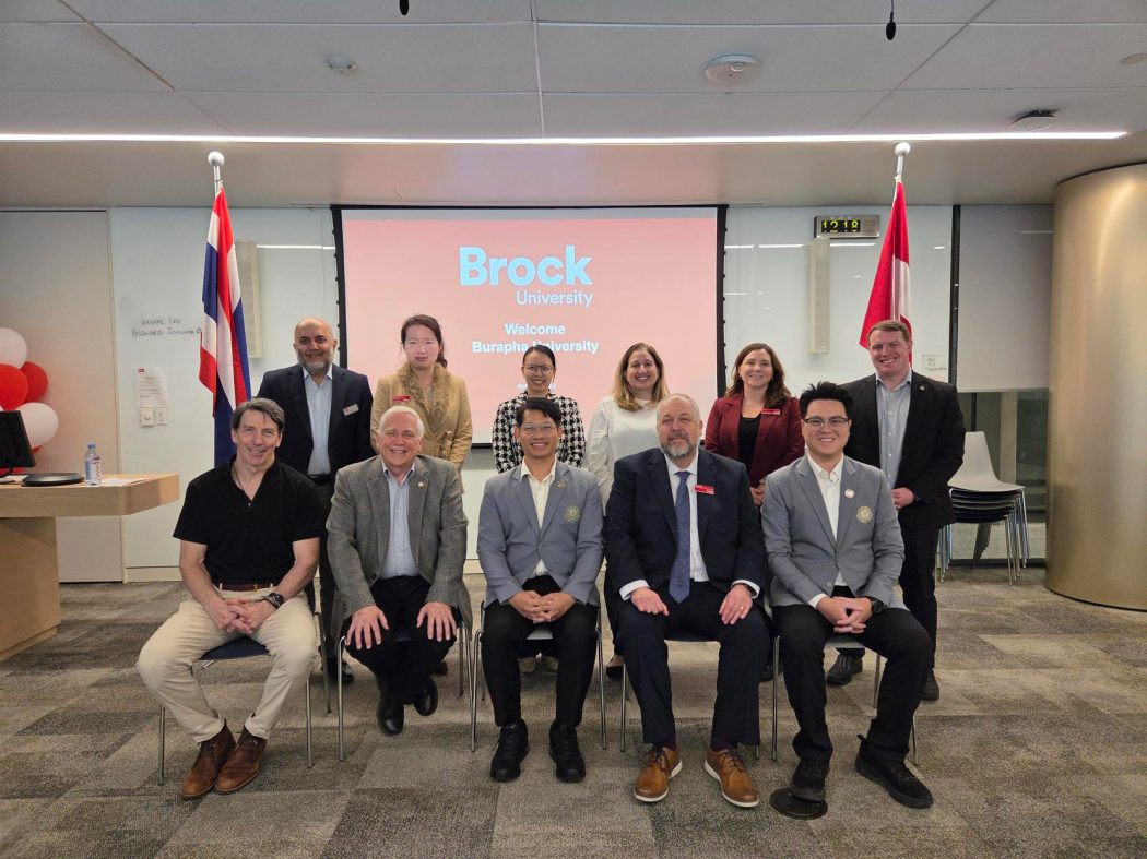 A group of seated and standing people pose for a photo in front of a presentation screen in a meeting room.