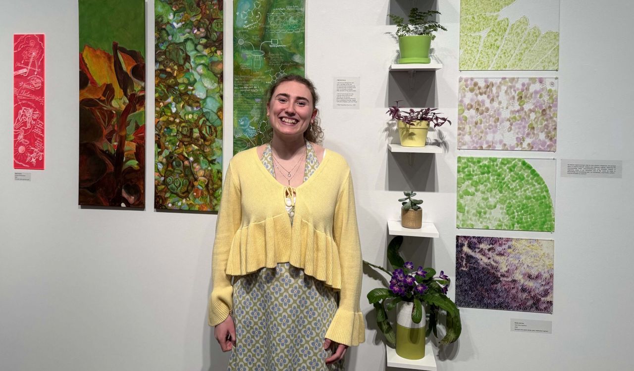 A young woman stands in front of several paintings in a gallery.