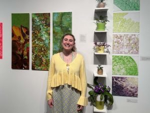 A young woman stands in front of several paintings in a gallery.