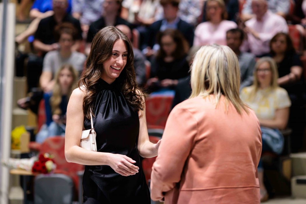 A young woman stands in front of a university professor on stage at a nursing pinning ceremony.