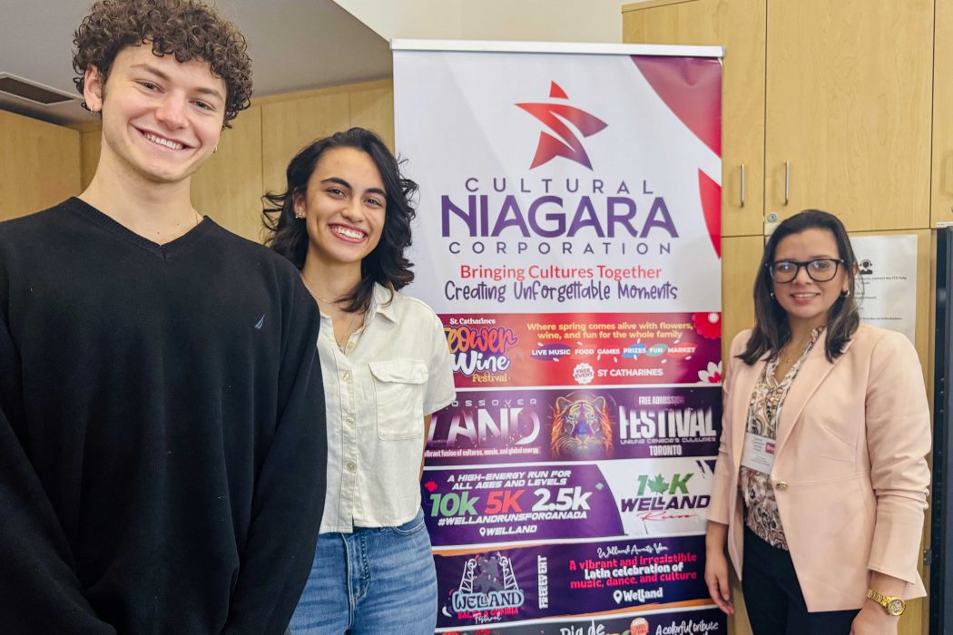 Three people stand together smiling with a colourful event banner. 