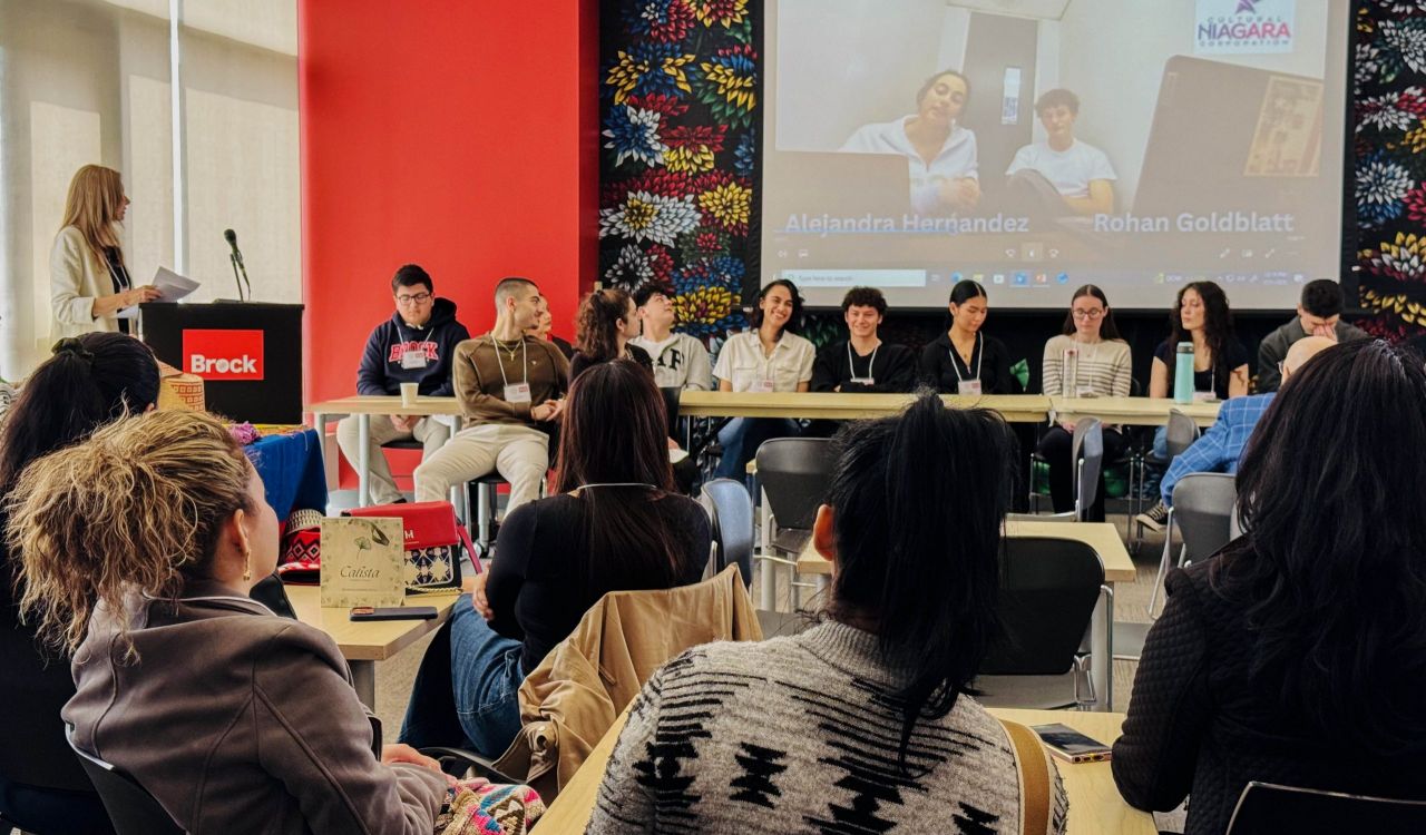 A group of people gather in a room and watch a video on a large projector screen.