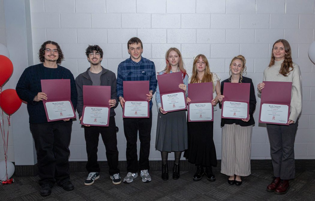 A group of seven students stand together each holding a certificate and smiling.