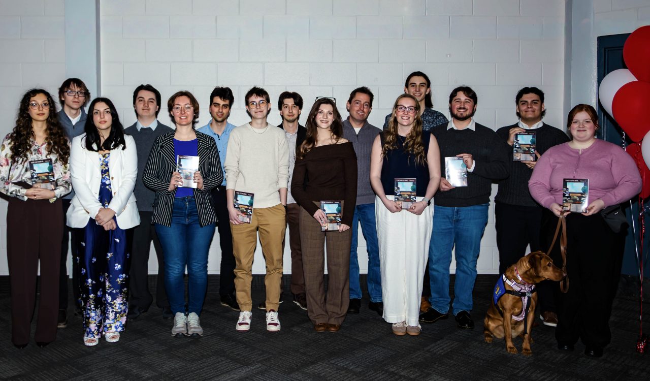 A group of smiling students stand together holding journals in their hands.