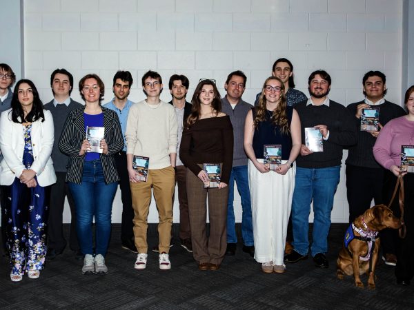 A group of smiling students stand together holding journals in their hands.