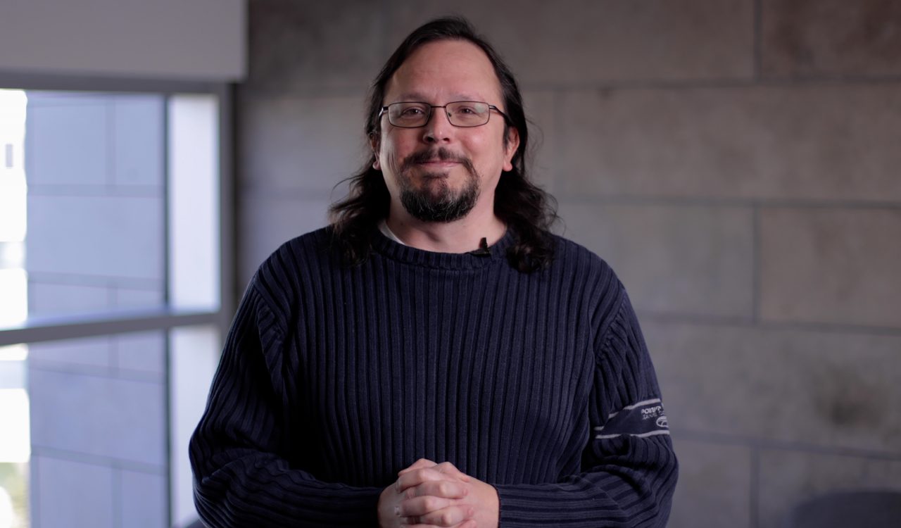 Portrait of Tony Volk standing in front of a concrete wall and window.