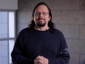 Portrait of Tony Volk standing in front of a concrete wall and window.
