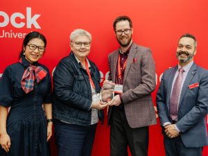 Four people pose with an award in front of a red backdrop.
