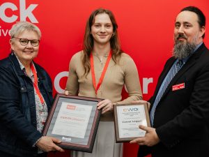 Three people pose with awards in front of a red backdrop.