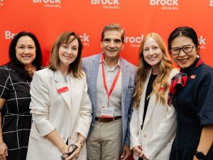A group of five people pose in front of a red backdrop.