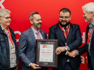 A group of four people pose with an award in front of a red backdrop.