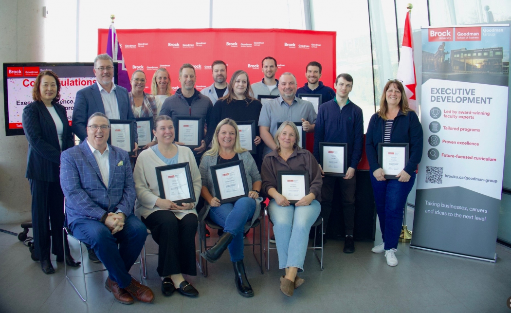A group of people holding certificates pose in front of a red backdrop.