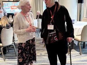 Two women stand together talking.