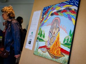 A colourful artwork is displayed on an easel beside a Health, Art and Justice Lab poster while attendees mingle in the background.