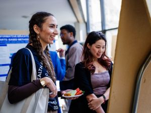 Attendees smile and chat while viewing poster displays at a Health, Art and Justice Lab gathering.