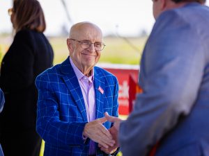 An older man wearing a blue plaid jacket and Brock University pin shakes hands with another attendee at an outdoor event.
