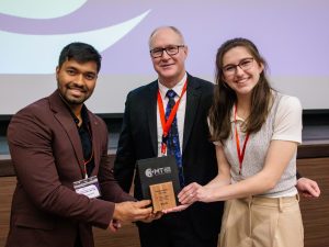 Three people stand together holding an award between the three of them.