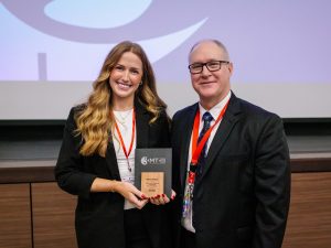 Two people stand together, one holding an award.