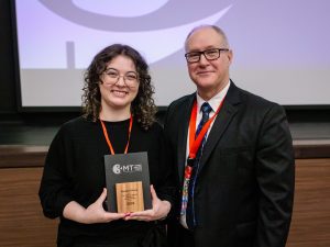 Two people stand together, one holding an award.