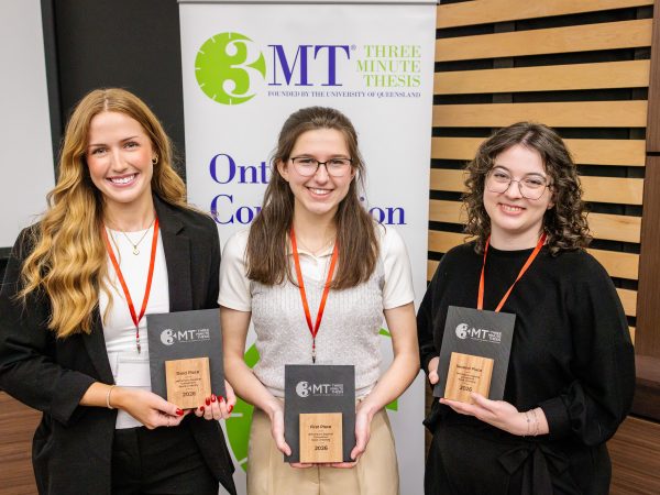 Three women stand together holding awards.