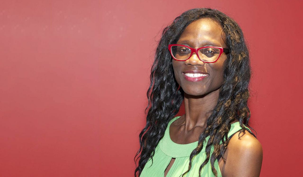 A woman poses for a photo against a red wall.