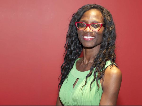 A woman poses for a photo against a red wall.
