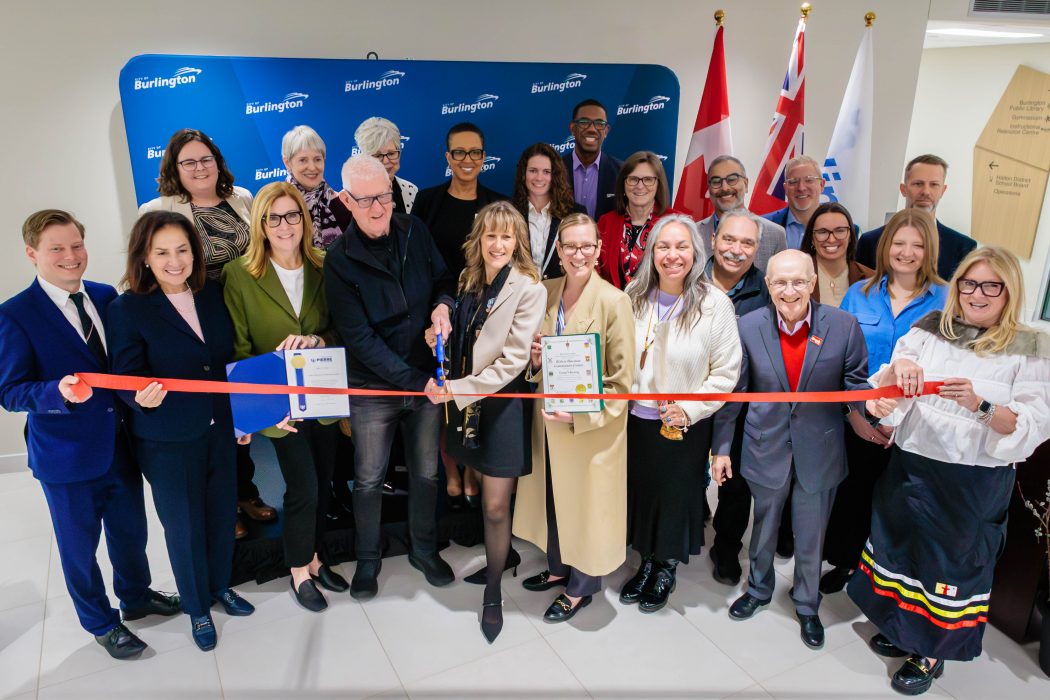 A large group of people pose behind a red ribbon and an opening ceremony for a community centre.