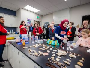 A group of people observe a child exploring a learning activity using shells and water in a classroom.