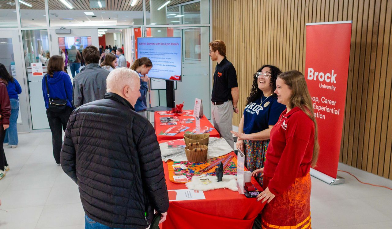 People stand together speaking over a table in a foyer with booths set up.