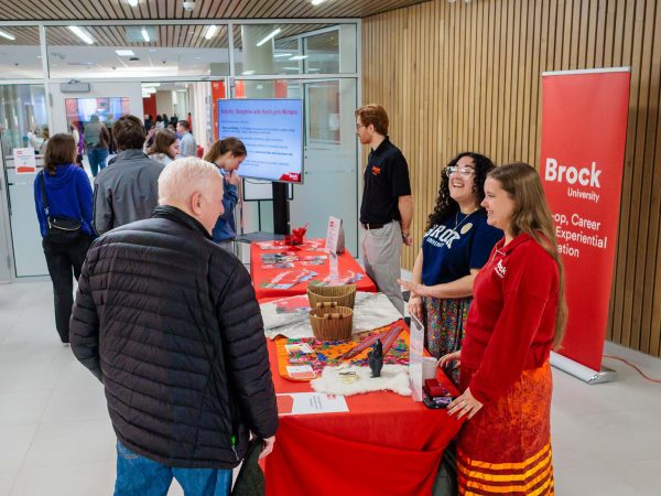 People stand together speaking over a table in a foyer with booths set up.