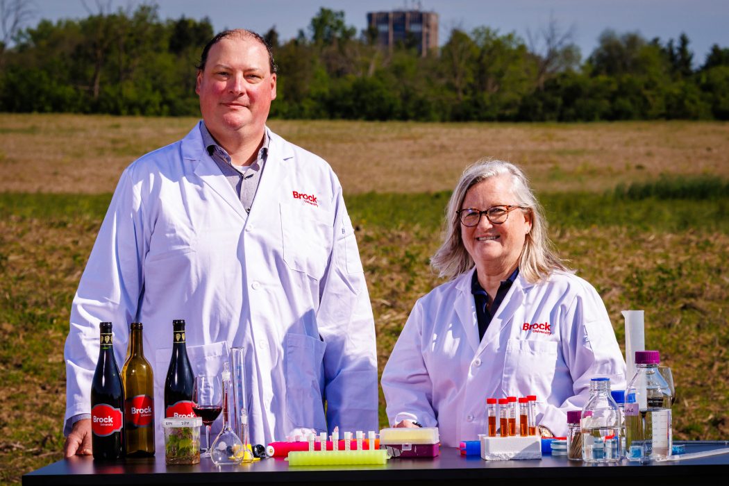 Two people in lab coats pose for a photo behind a table in a field.