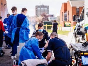 Nursing students and Niagara EMS paramedics work together around a simulated patient on a stretcher near an ambulance during a Code Orange exercise.