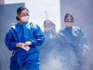 Nursing students in blue protective gowns move through smoke as part of an outdoor emergency response simulation.