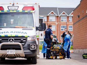 Ambulance parked near nursing students and paramedics gathered around a stretcher during a Code Orange emergency simulation.