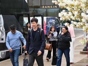 A man smiles while walking away from a bus in front of other people.