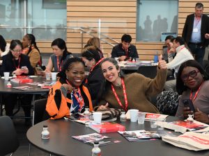Two women smile while sitting at a table during an event at a university.