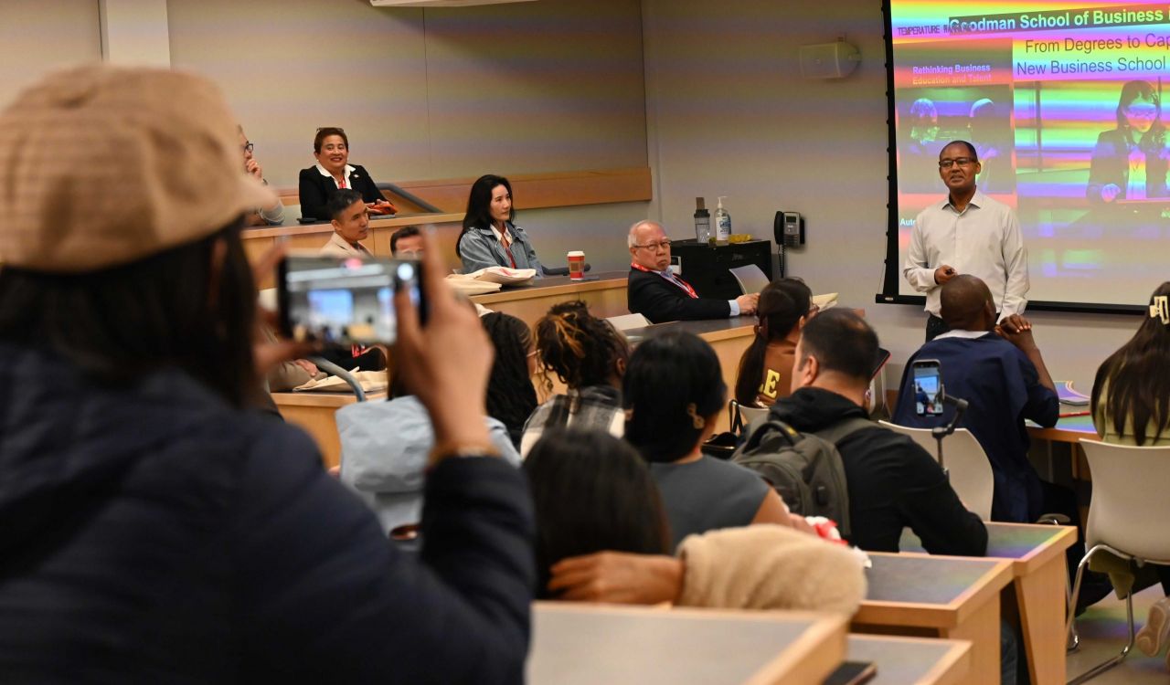 An audience listens to someone speaking from the front of a university lecture hall.