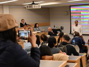 An audience listens to someone speaking from the front of a university lecture hall.