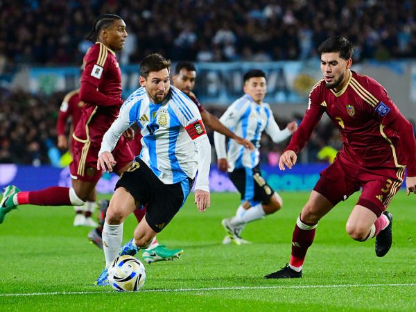 Soccer players from two teams on a green soccer pitch, one controlling the ball as others attempt to intervene.