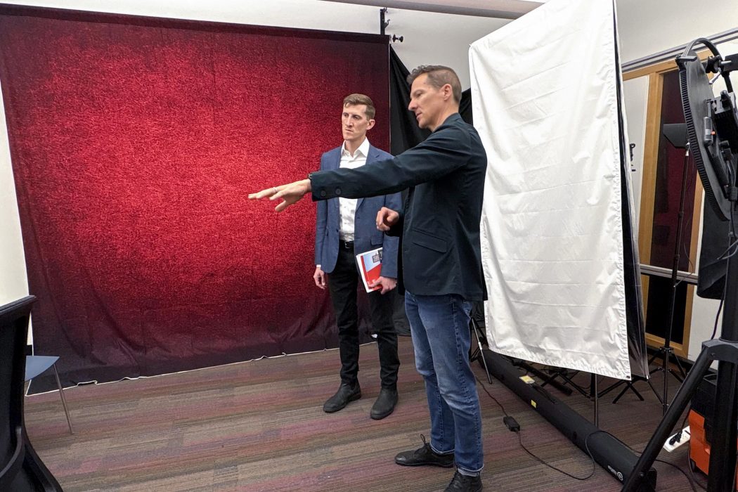 Two people look at technical equipment with various video and photo backgrounds behind them.