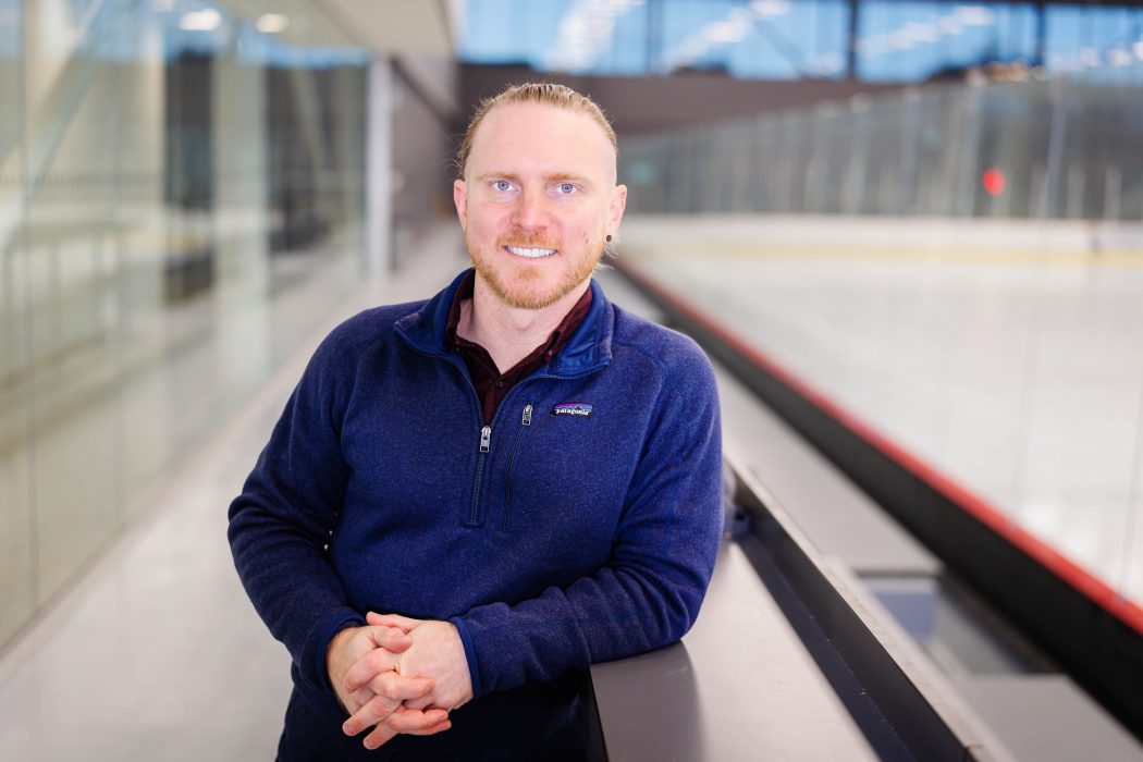 Brock University Associate Professor of Sport Management Kyle Rich leans on the boards of an ice rink.