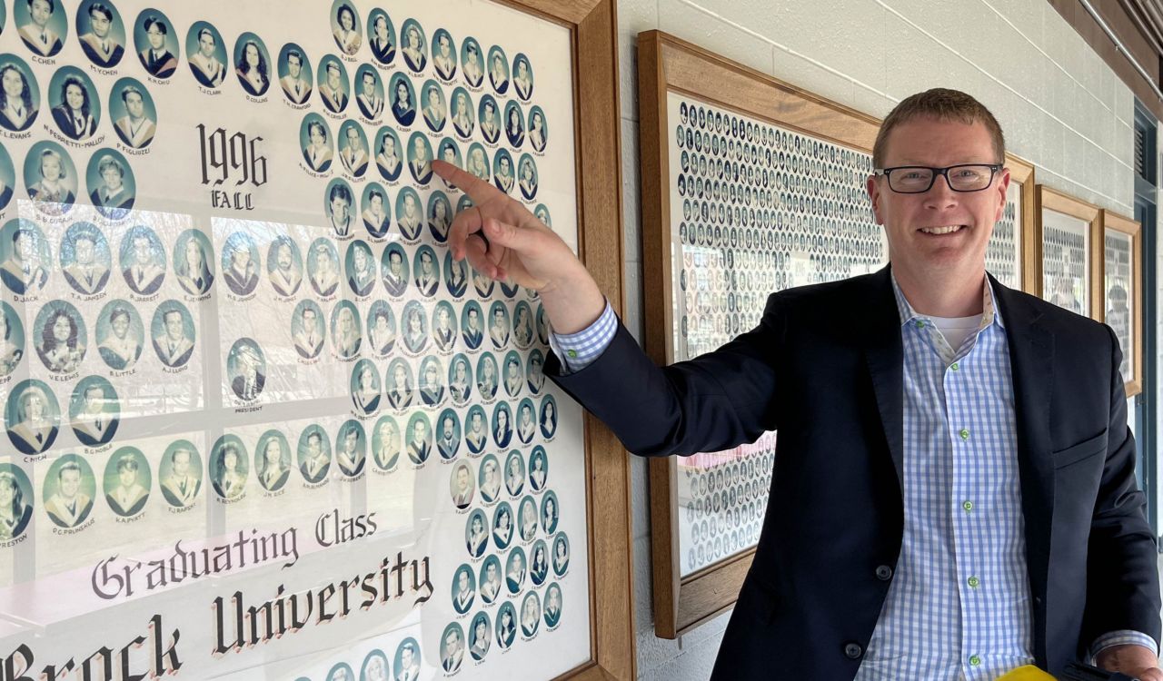 A man looking at his class photo on a university campus.