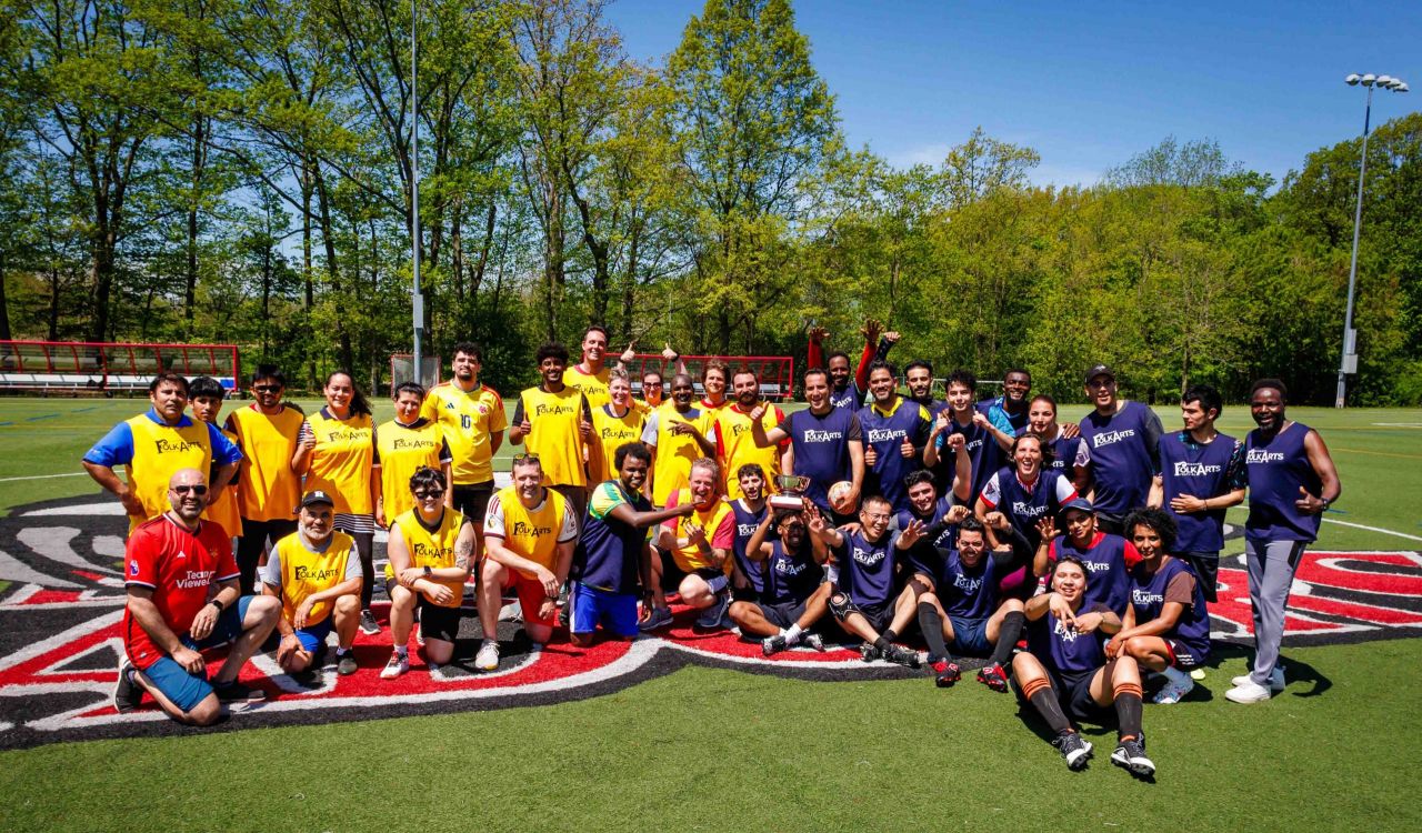 A large group of people in soccer uniforms pose for a photo in a field.