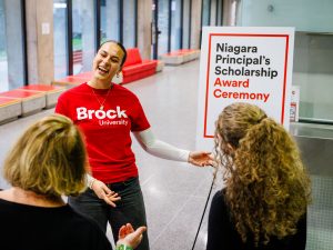 A Brock University student ambassador welcomes guests near a Niagara Principal’s Scholarship Award Ceremony sign.
