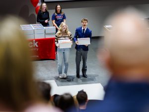 Two Niagara Principal’s Scholarship recipients smile on stage while holding their Brock welcome boxes.